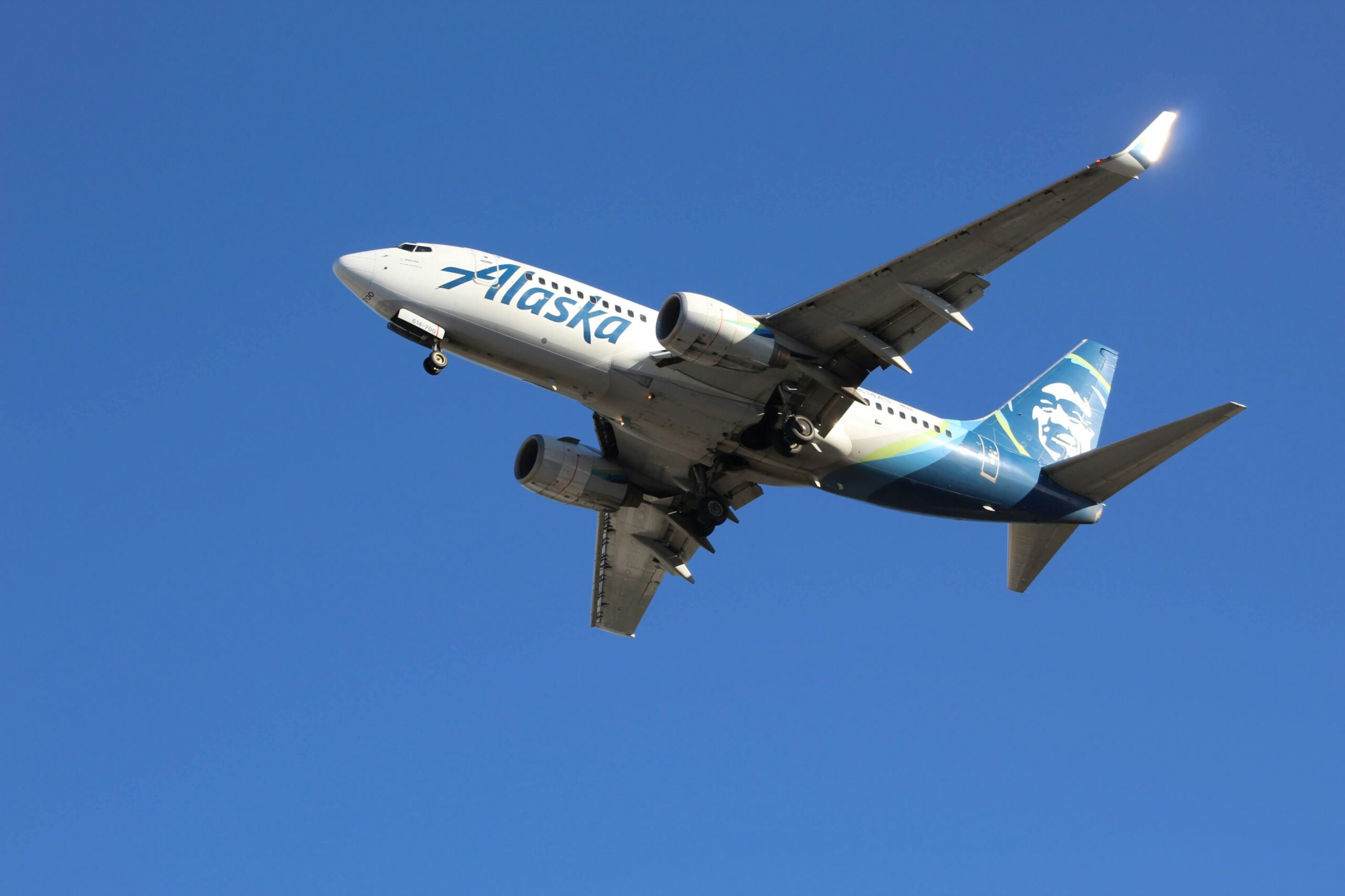 Alaska Airlines airplane cruising under a clear blue sky.